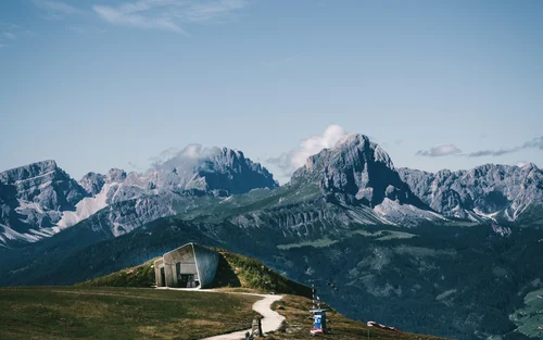 Sentiero che conduce a una baita moderna tra le montagne sotto un cielo blu