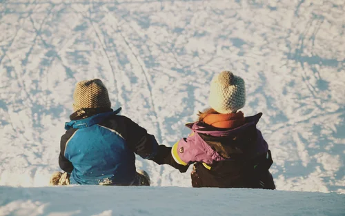 Due bambini con abbigliamento invernale seduti sulla neve che si tengono per mano