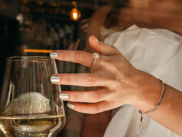 Frau mit silbernen Nägeln und Schmuck hält Weinglas mit Weißwein