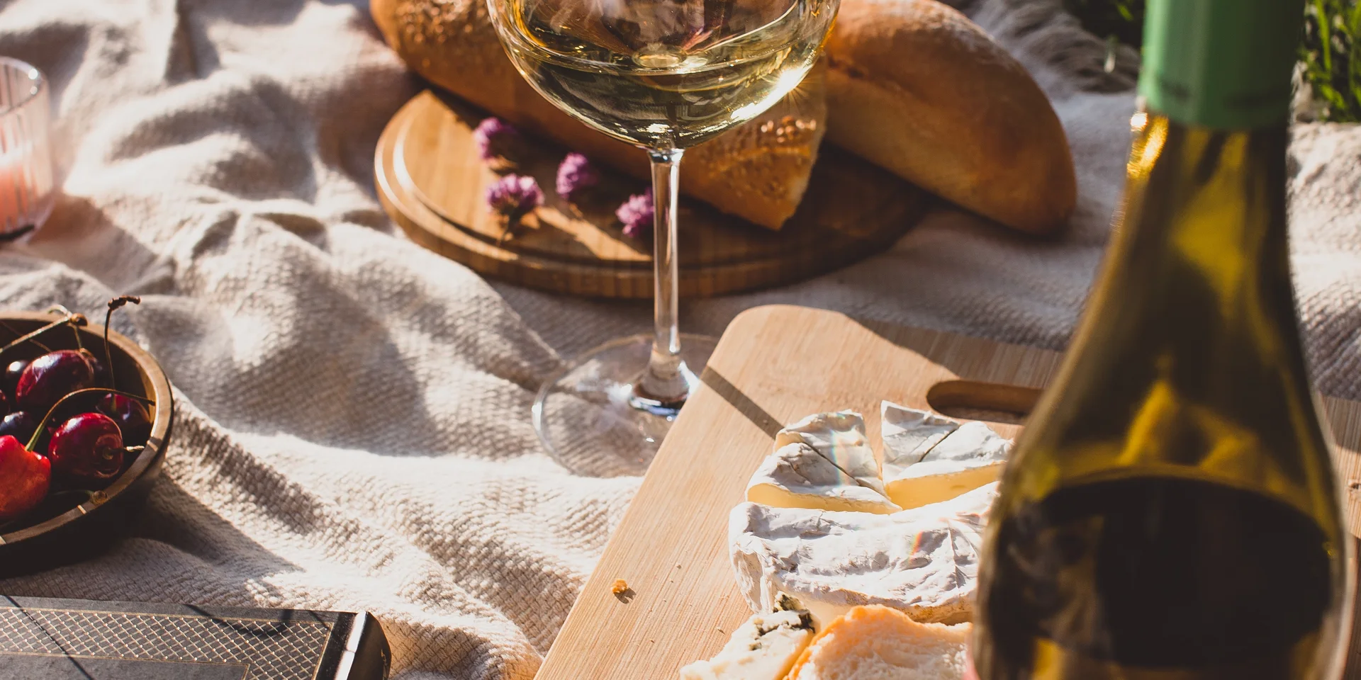 Picknick mit Weißwein, Käse, Brot und Kirschen auf einer Decke im Gras