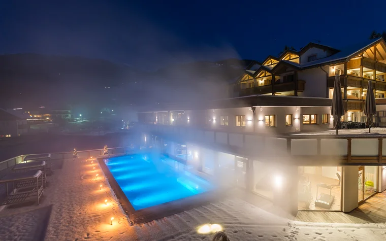Absolutely stunning impressions Lit outdoor pool with steam beside snow-covered hotel at night