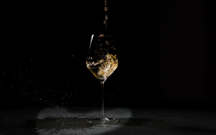 Weißwein, der in ein Weinglas vor schwarzem Hintergrund eingeschenkt wird