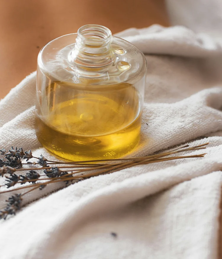 Bottle of essential oil with lavender sprigs on white towel