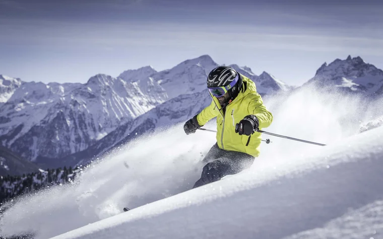 Da cartolina, queste immagini Sciatore con giacca giallo neon scende sulla neve fresca davanti a montagne innevate