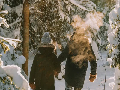 Zwei Personen gehen im schneebedeckten Wald bei Sonnenlicht spazieren