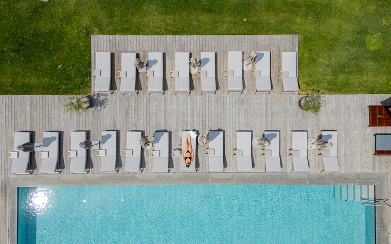 Frau liegt auf Liegestuhl neben Pool mit weiteren Liegestühlen und Rasen