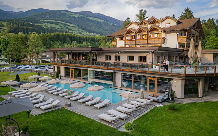 Hotel mit Außenpool, Liegestühlen und Bergen im Hintergrund