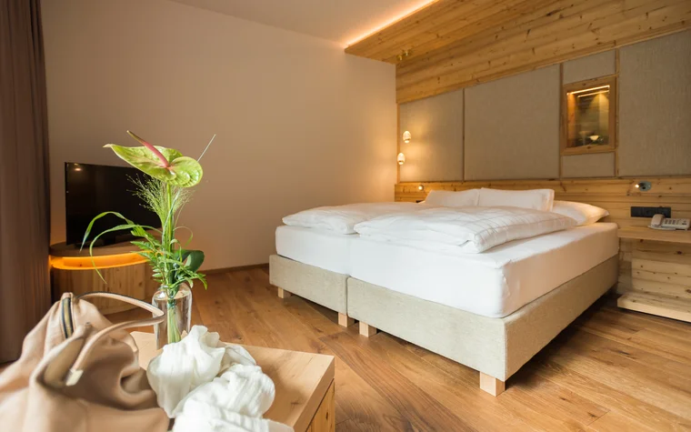 Gemütliches Hotelzimmer mit Doppelbett, Holzmöbeln und grüner Pflanze