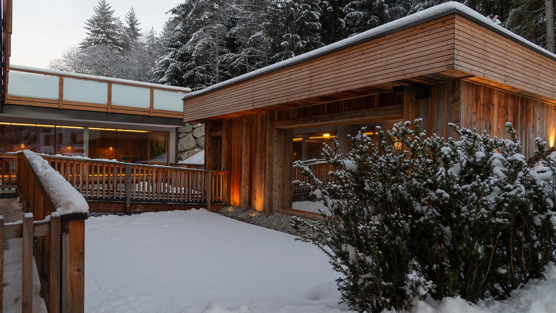 Green Lake Hotel Weiher: das 4-Sterne-Superior-Hotel im Pustertal Holzhaus mit verschneitem Garten und Büschen vor verschneitem Wald
