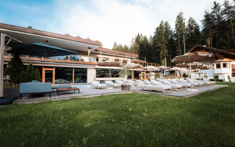 Liegestühle und Sonnenschirme auf Terrasse vor modernem Hotel mit Wald im Hintergrund