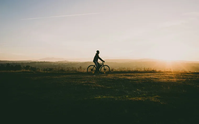 Person mit Fahrrad bei Sonnenuntergang auf offenem Feld