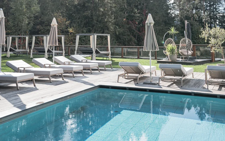 Pool mit Liegestühlen und Sonnenschirmen vor Waldkulisse bei Tageslicht