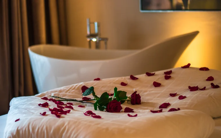 Rosenblätter und eine Rose auf einem weißen Bett vor einer Badewanne