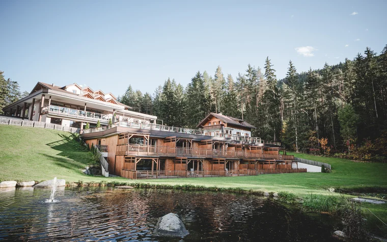 Holzhaus und Hotelgebäude am See mit Wald im Hintergrund