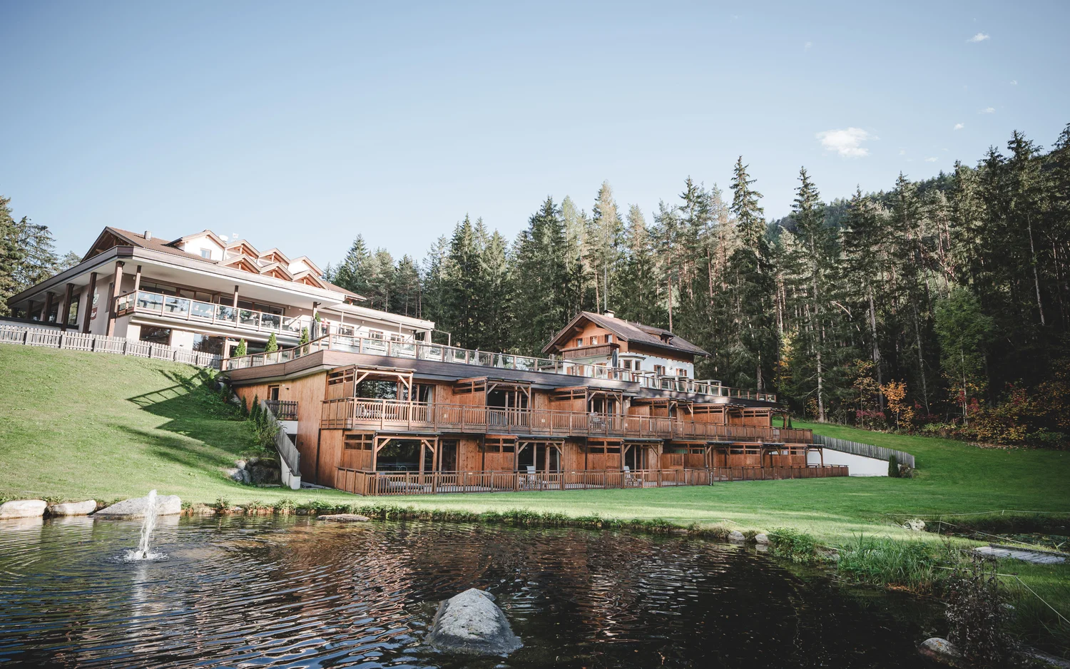 Holzhaus und Hotelgebäude am See mit Wald im Hintergrund