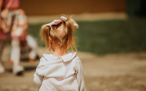 Bambina con codini e fiocco rosa vista da dietro all'aperto