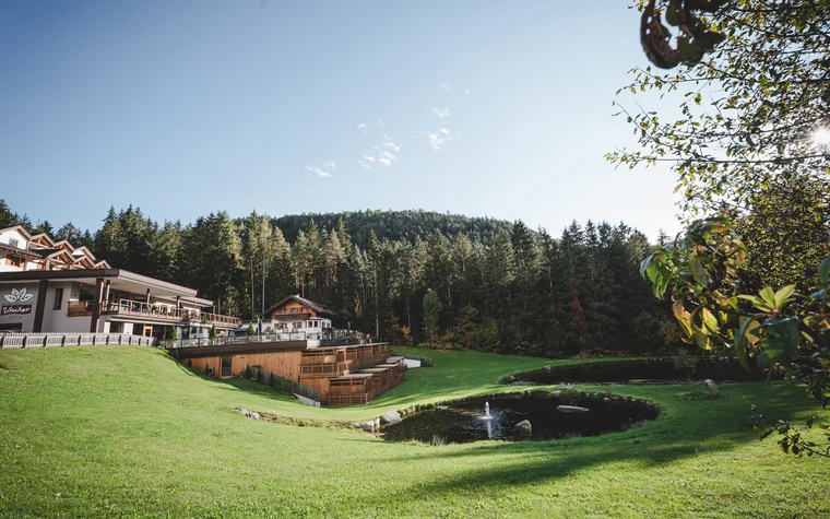Hotelgebäude mit Terrasse neben Teichen und Wald unter klarem Himmel