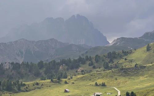 Colline verdi con alberi e case sotto un cielo nuvoloso e montagne sullo sfondo