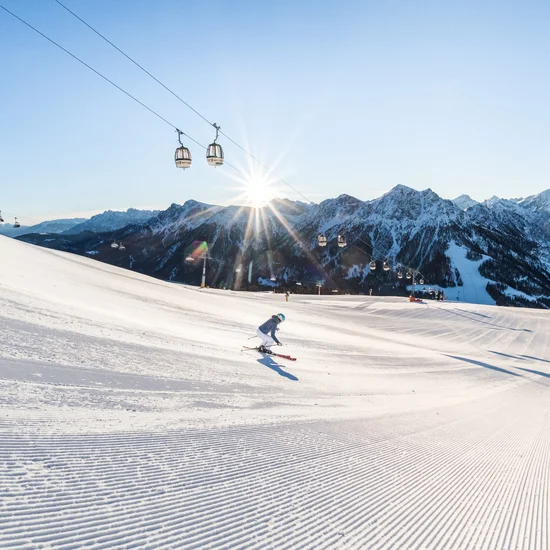 Sonnenskitage Neujahr Zwei Skifahrer auf einer sonnigen Piste mit Bergpanorama und Gondelbahn