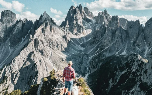 Vacanze sportive sulle Dolomiti: tra vetta e laghetto Escursionista con cane su sentiero di montagna davanti a picchi rocciosi sotto cielo azzurro