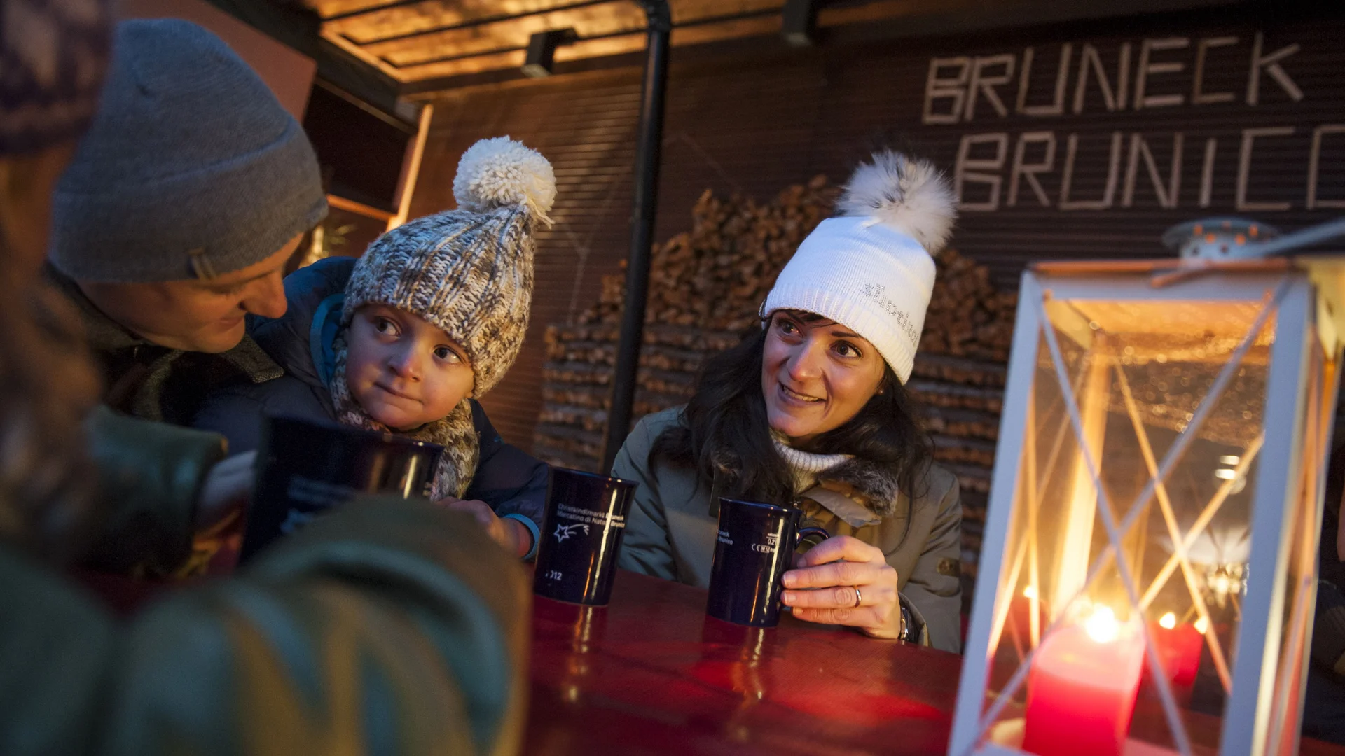 Traditionen & Bräuche in Südtirol zu Weihnachten und Silvester Familie mit Wintermützen trinkt heiße Getränke an einem Tisch mit Laterne