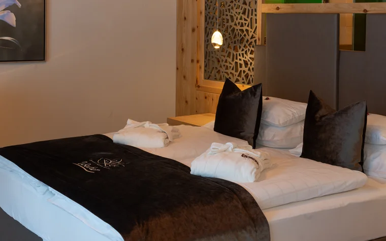 Gemütliches Hotelzimmer mit großem Bett, schwarzen Kissen und weißen Bademänteln