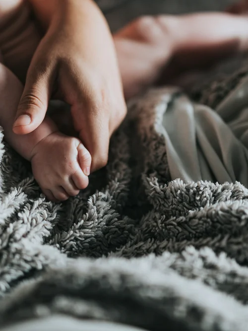 Erwachsener hält die Hand eines Babys auf einer weichen grauen Decke