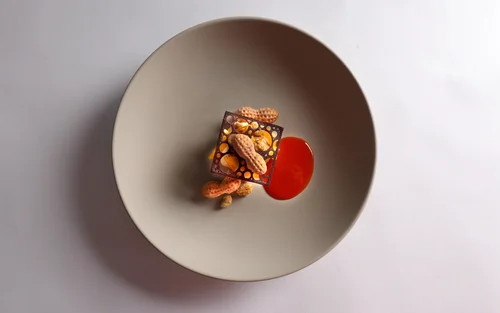 Kunstvoll angerichtetes Dessert mit Erdnüssen und roter Sauce auf grauem Teller