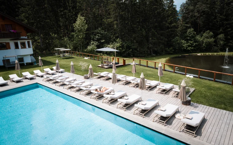 Pool mit Liegestühlen und Sonnenschirmen neben einem Teich und Wald