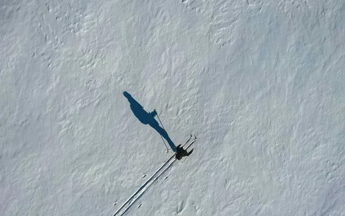 Drohnenaufnahme eines Skifahrers auf schneebedecktem Hang mit langem Schatten