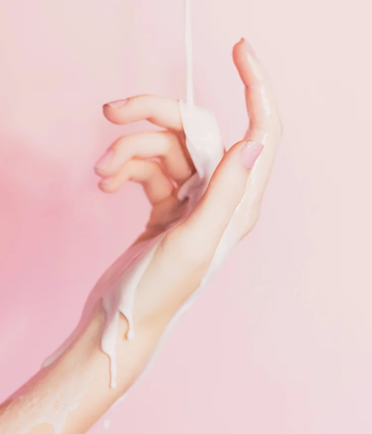 Hand with flowing white liquid against pink background