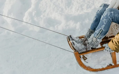 Person mit schneebedeckten Stiefeln auf einem Holzschlitten im Schnee