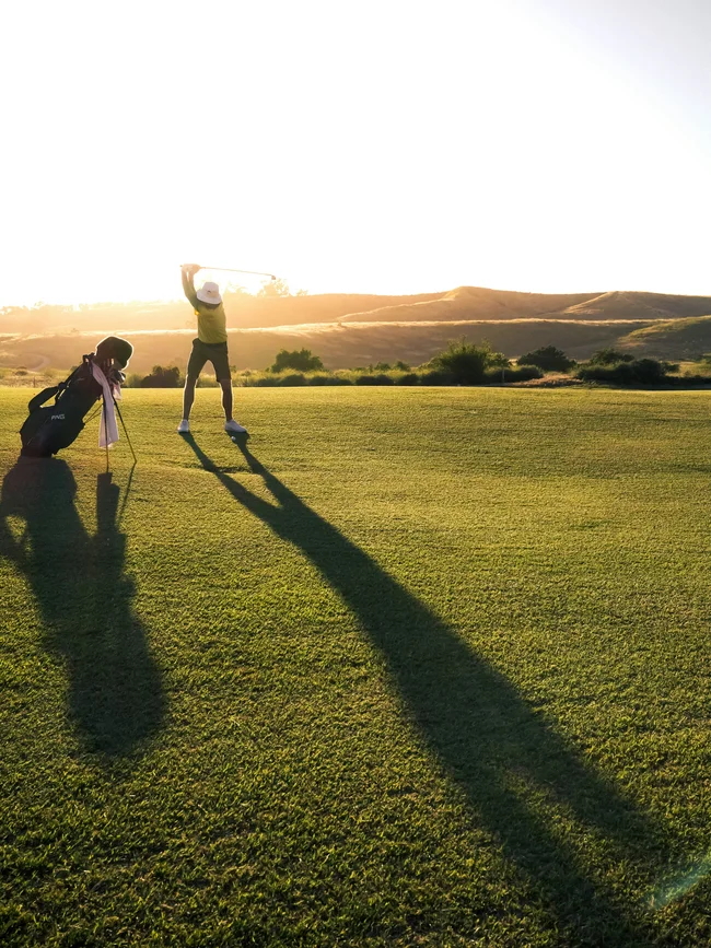 Golfer schlägt Ball auf sonnigem Golfplatz mit langer Schatten