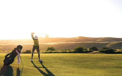 Golfer schlägt Ball auf sonnigem Golfplatz mit langer Schatten