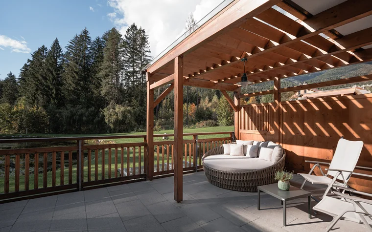 Terrasse mit Holzdach, runder Lounge und Liegestühlen vor Waldkulisse
