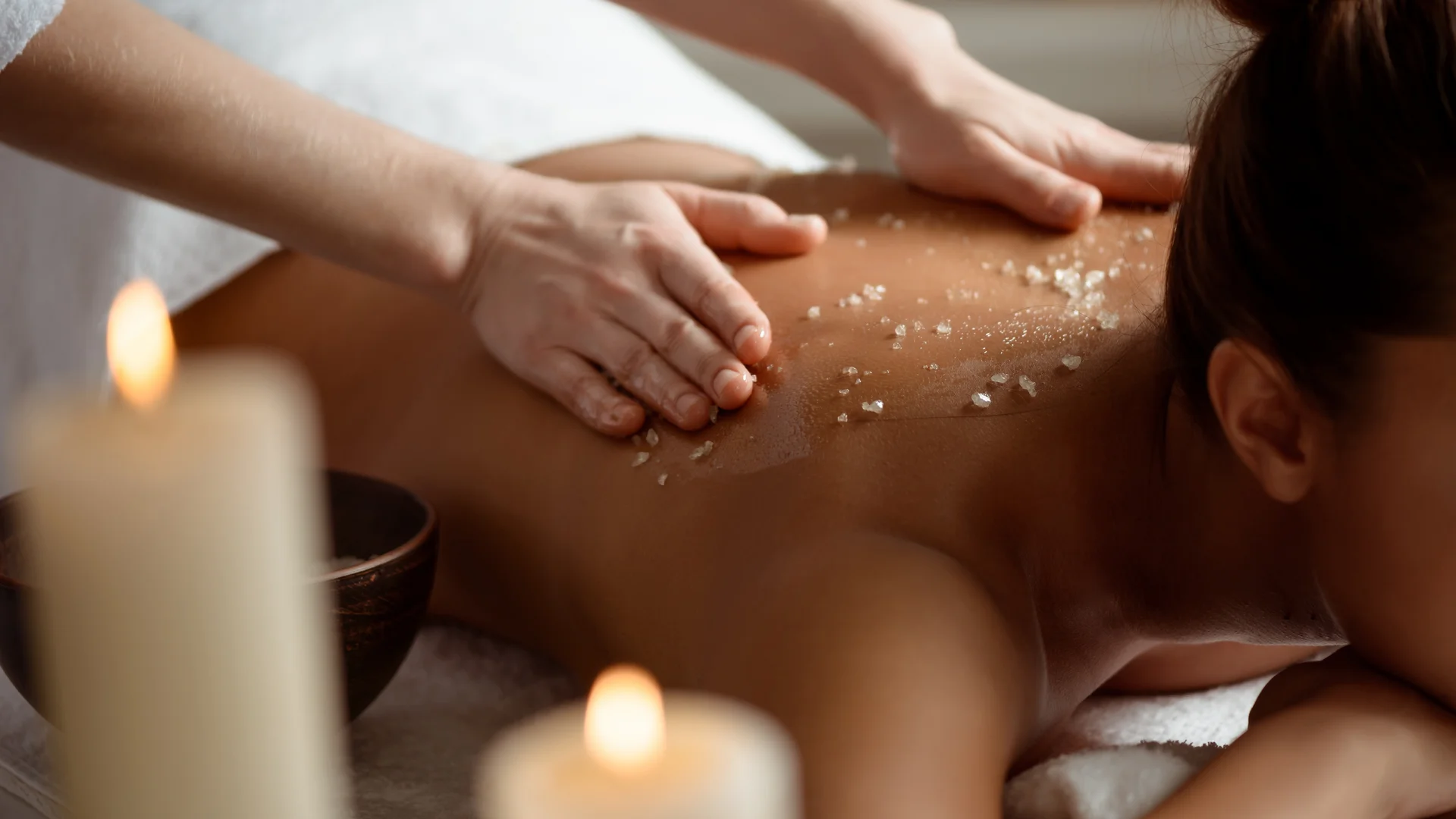 Woman receiving back massage with scrub in a relaxing spa setting