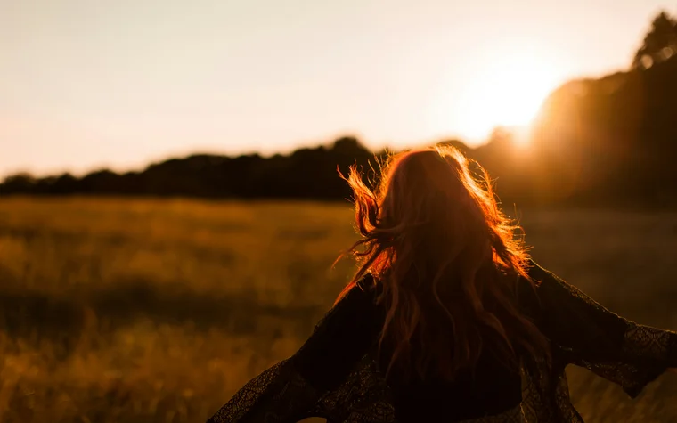 Frau mit roten Haaren läuft bei Sonnenuntergang durch ein Feld