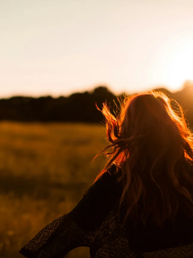 Frau mit roten Haaren läuft bei Sonnenuntergang durch ein Feld